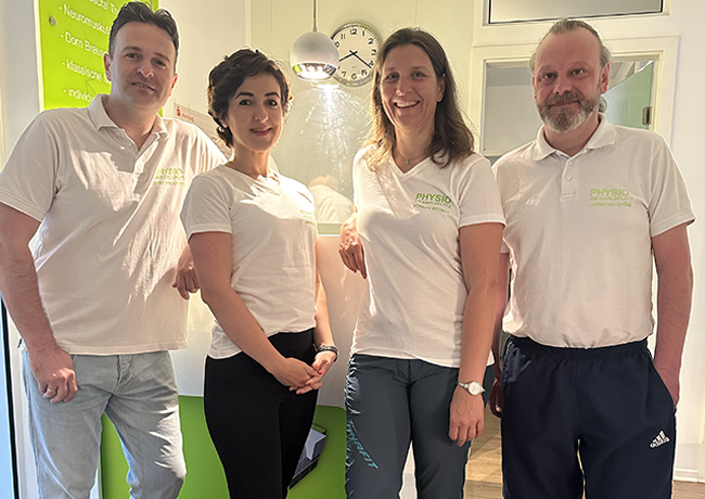Zwei Therapeutinnen und zwei Therapeuten in weißen Poloshirts posiert nebeneinander im hellen Eingangsbereich.